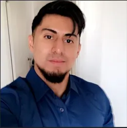Portrait of mature man with white beard smiling outdoors on urban street with parked cars and buildings in the background.